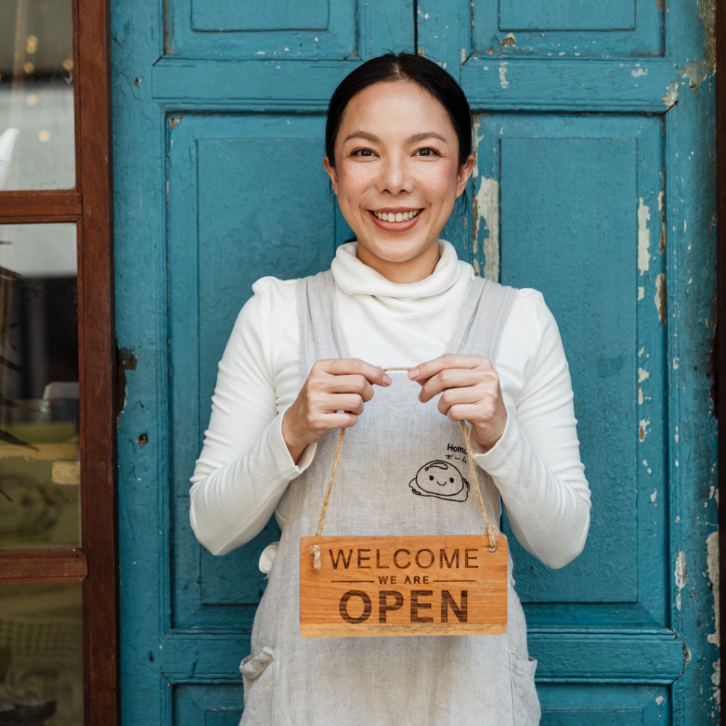A small business owner holding a welcome we're open sign in front of her door.