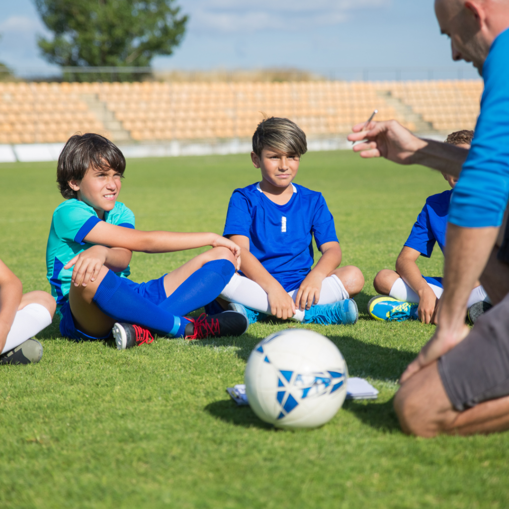 Boys sitting down at soccer practice listening to their coach.