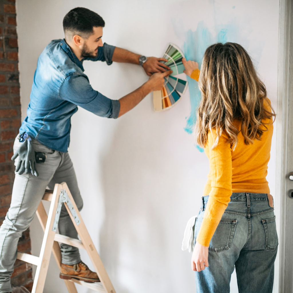 A couple holding paint swatches against a wall as they choose a new paint color.